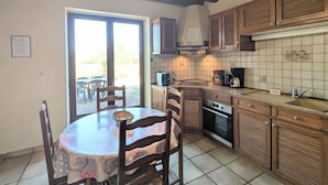 A kitchen with wooden cabinets, a tiled backsplash, and a dining area with a table and chairs. - Countryside home near Châteauroux, family-friendly (Arthon)