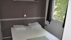 A small, single-bed room with a window, a bedside table, and a wardrobe. - Spacious mobile home for 8 with terrace (Lavilledieu)