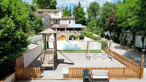 A playground with a wooden slide and swings, surrounded by a fence and trees. - Spacious mobile home for 8 with terrace (Lavilledieu)