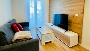 A modern living room with a grey sofa, a white coffee table, and a flat-screen TV on a wooden accent wall. - Modern Studio in Candanchú, 4 ppl, 2 beds (Aisa-Candanchú)