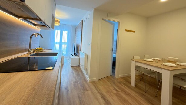 A modern kitchen with a central island, a dining area with a table and chairs, and a view of the living area through an open door. - Modern Studio in Candanchú, 4 ppl, 2 beds (Aisa-Candanchú)