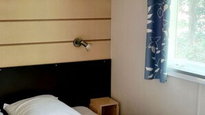 A bed with white bedding, a wooden headboard, a small wooden nightstand, and a window with a blue curtain. - Comfortable Mobile Home for 4 pers. with Terrace (Espira-de-Conflent)