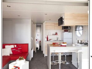 Ein kompakter Wohnraum mit Küchenzeile, einer Essecke mit Barhocker und einem roten Sofa mit weißem Tisch.