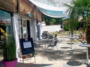 Un área de estar al aire libre con mesas y sillas, un letrero y una planta en maceta.