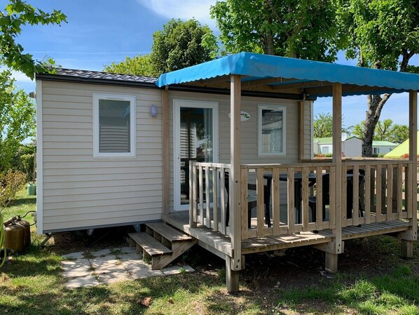 Una casa móvil con terraza de madera y toldo azul.