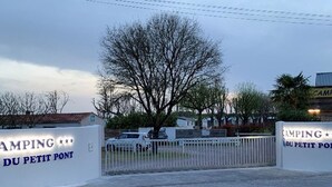 Un cancello chiuso all'ingresso di un campeggio chiamato "Camping du Petit Pont", con una recinzione bianca e un albero sullo sfondo.