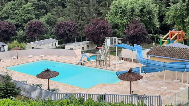 Ein Schwimmbad mit Rutsche und Wasserspielbereich, umgeben von Bäumen und einigen Gebäuden.