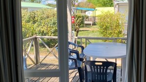 A covered outdoor area with a wooden deck, a round table, and two chairs. - Cosy mobile home with terrace for 4 (Arvert)