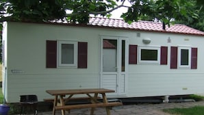 A small, single-story mobile home with a tiled roof and a stone patio.