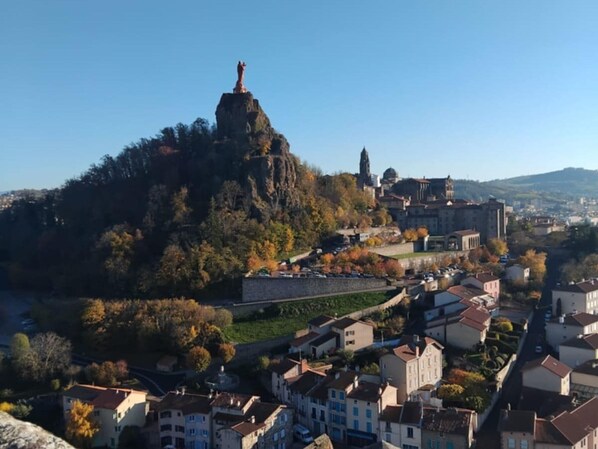 A town with a prominent statue on a hill, surrounded by buildings and a river. - Charming Apartment in the Heart of Le Puy-en-Velay (Le Puy-en-Velay)