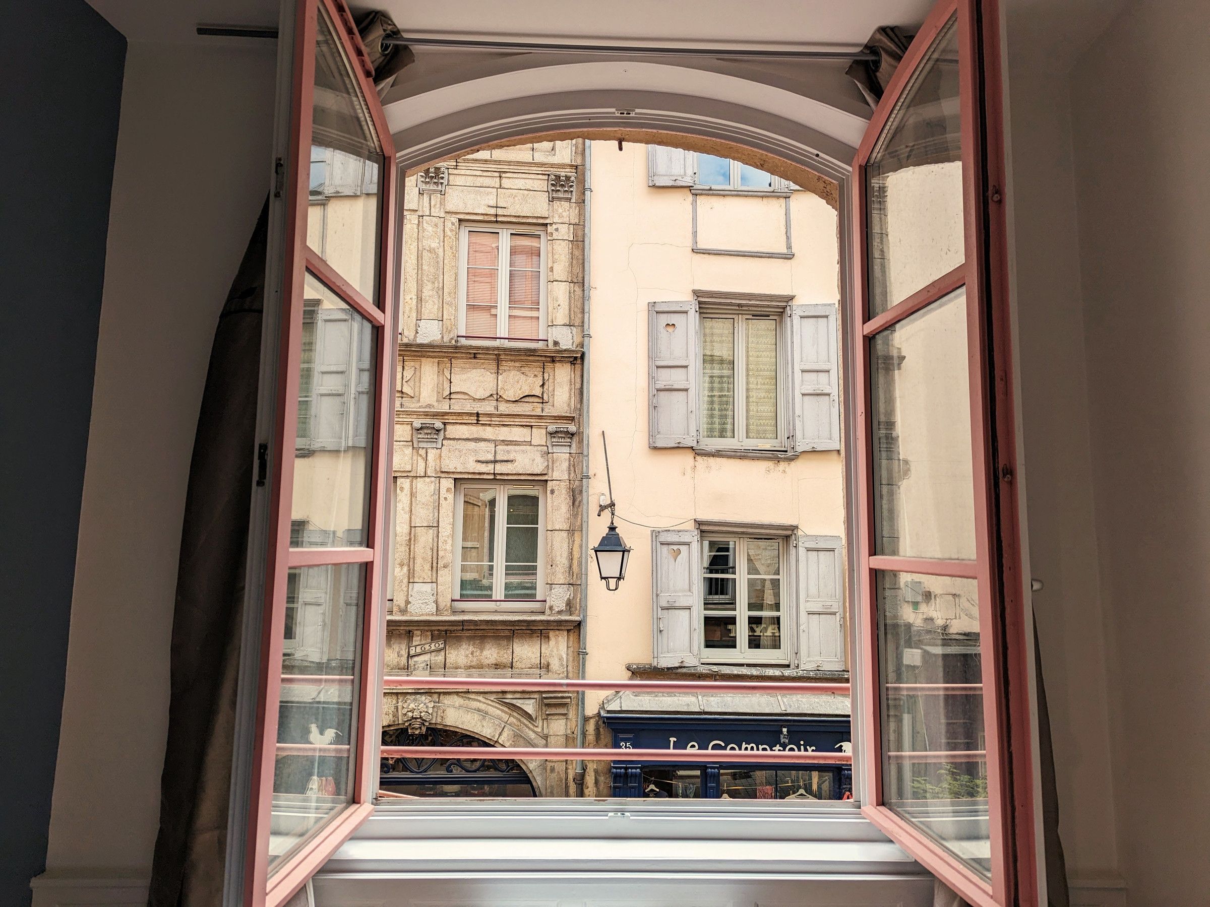 An open window with a view of a building with multiple windows and shutters.
