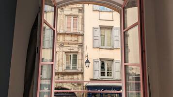 An open window with a view of a building with multiple windows and shutters.