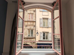 An open window with a view of a building with multiple windows and shutters.