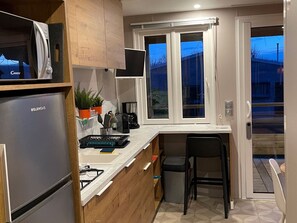 Eine kompakte Küche mit Kühlschrank, Mikrowelle und einem Fenster mit Vorhängen.