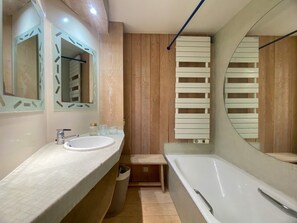 Ein modernes Badezimmer mit großem Spiegel, Waschbecken, Badewanne und Holzvertäfelung.