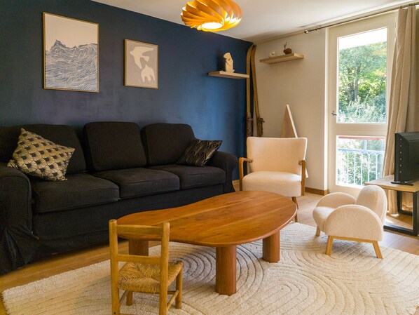 Ein Wohnzimmer mit einem dunkelgrauen Sofa, einem Holztisch, einem weißen Sessel und einem Fernseher auf einem Schrank.