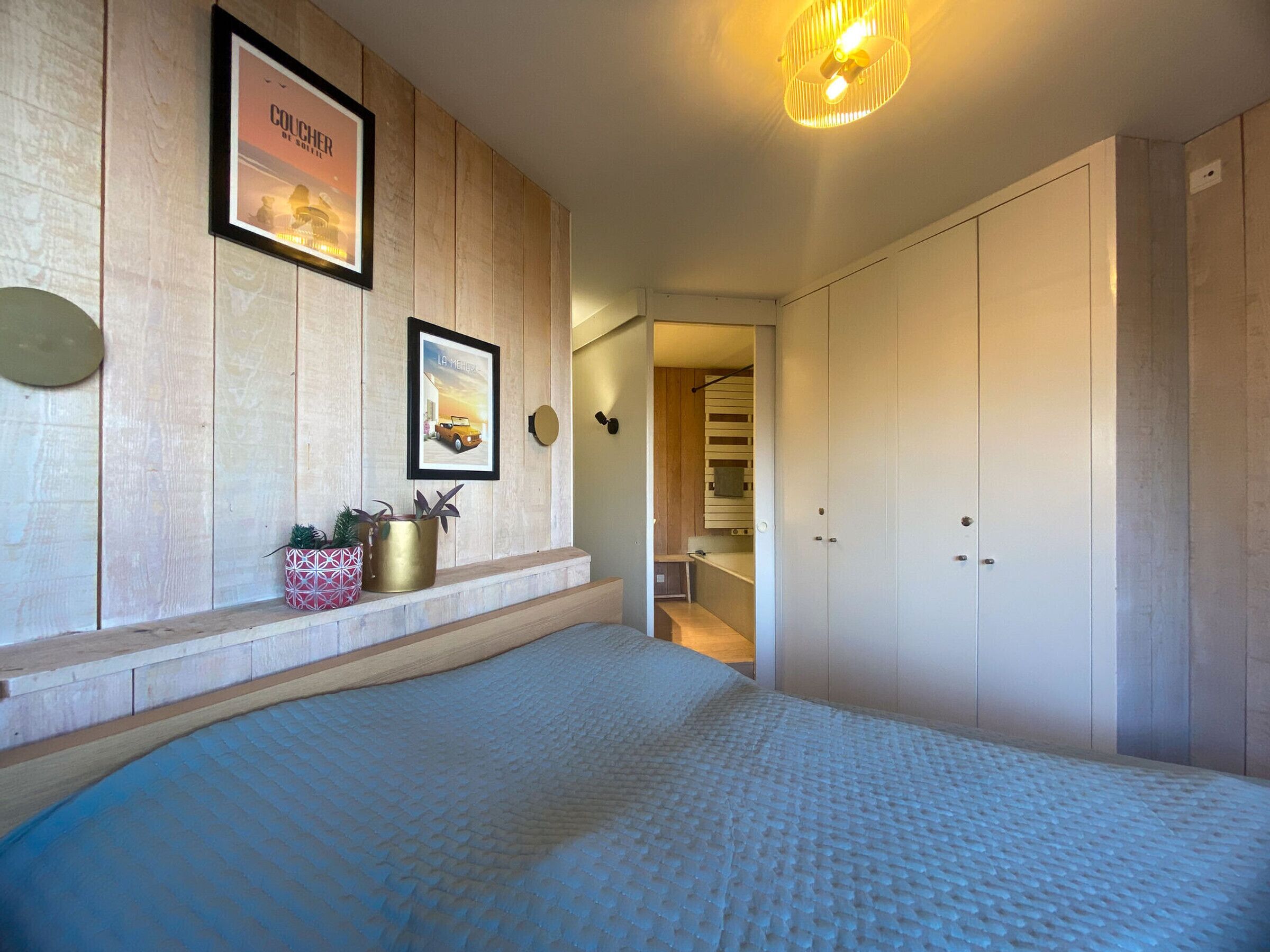 A bedroom with a large bed, wooden panel walls, a framed picture, and a hallway leading to a closet.