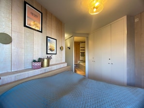 Ein Schlafzimmer mit einem großen Bett, Holzwandverkleidung, einem gerahmten Bild und einem zur Garderobe führenden Flur.