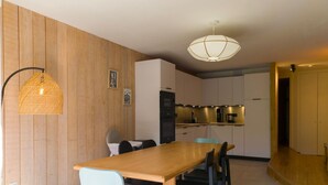 Ett modernt kök med väggar beklädda med träpaneler, ett matbord med stolar och en hänglampa.