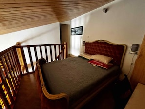 A bedroom with a wooden bed frame, a red headboard, a single bed with a grey bedspread, a nightstand with a lamp, and a window with a view of the outside. - Quiet house in La Terrière, near beach and shops (La Tranche-sur-Mer)
