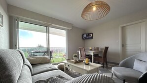 Een moderne woonkamer met een bank, een eettafel voor vier personen en een aan de muur bevestigde televisie.