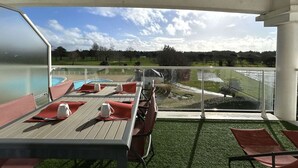 Een terras buiten met een pooltafel, stoelen en uitzicht op een golfbaan.