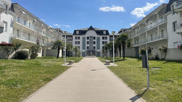 Een modern appartementencomplex met een centraal gelegen ingang, omringd door verzorgde gazons en palmbomen.