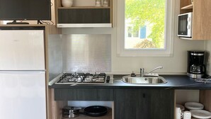 A compact kitchen with a gas stove, a sink, and a microwave. There is a window providing natural light and a view of greenery outside.