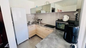 Una cocina compacta con refrigerador, pileta, mostrador, horno y cafetera.