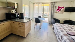 Habitación de hotel compacta con kitchenette, zona de comedor, cama y balcón con vistas.