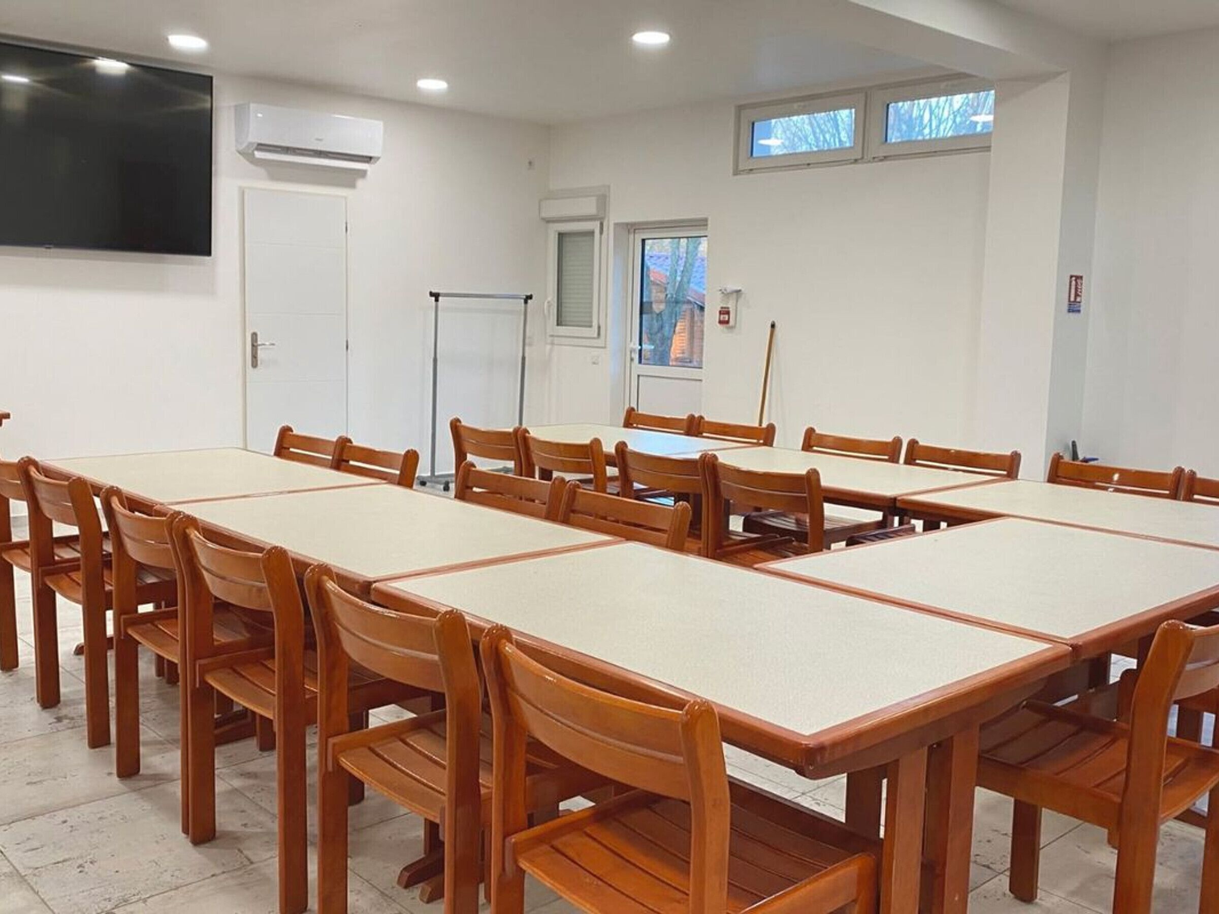 A conference room with a long table and chairs, white walls, and a large flat-screen TV.