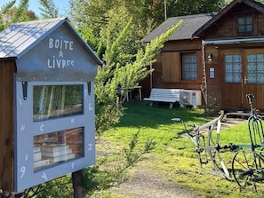 En stuga av trä med ett litet bibliotek som har skylten ”BOITE A LIVRES” och ett cykelställ.