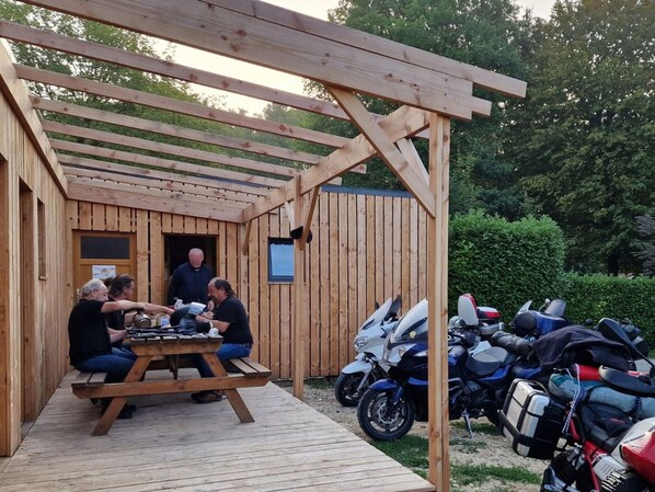 Un pabellón de madera con una mesa de picnic y motocicletas estacionadas afuera.