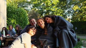 A group of people sitting at an outdoor table with a wooden fence and greenery in the background.