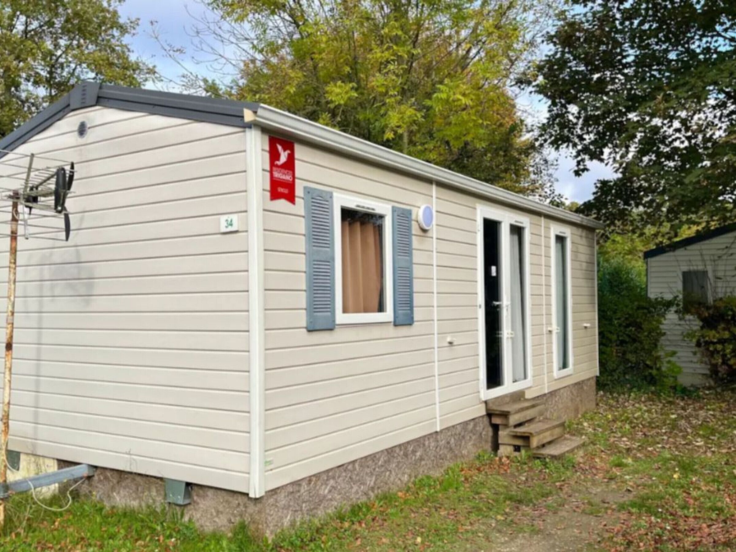 A single-story mobile home with a beige exterior, a small porch, and a red flag on the side.