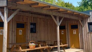 A wooden cabin with a covered porch, picnic tables, and yellow doors.