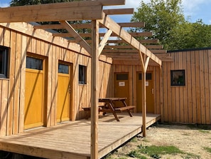Una cabaña de madera con un porche, una mesa de picnic y dos puertas.