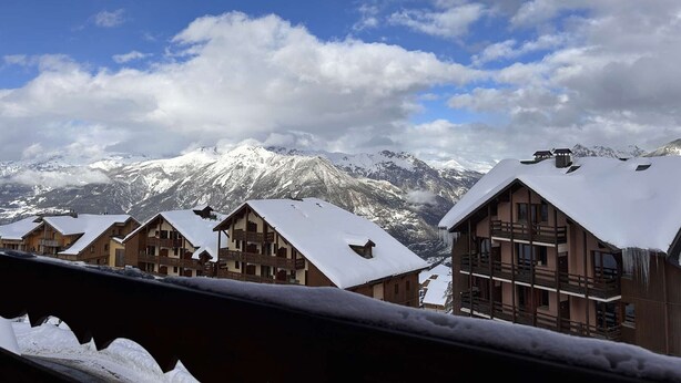 A row of wooden chalets with snow-covered roofs, set against a backdrop of snow-capped mountains and a partly cloudy sky. - Apartment at slopes, Wifi included, sauna, 5 sleeps (Risoul)