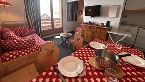 A cozy room with a bed, a dining table set with plates, glasses, and a pan, a small wooden chair, a television, and a kitchen area. - Apartment at slopes, Wifi included, sauna, 5 sleeps (Risoul)