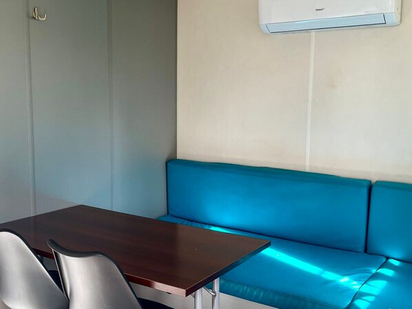 A corner of a room with a dark wooden table, a blue cushioned bench, and a wall-mounted air conditioner.