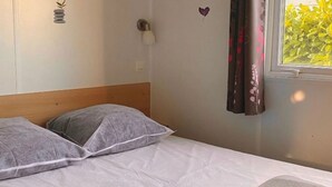Ein Einzelbett mit Holz-Kopfstück, einer weißen Bettdecke und zwei grauen Kissen.