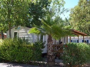 A small, single-story cabin with a porch, surrounded by dense greenery and a palm tree. - Spacious mobile home with terrace, ideal for 8 people (Vias)