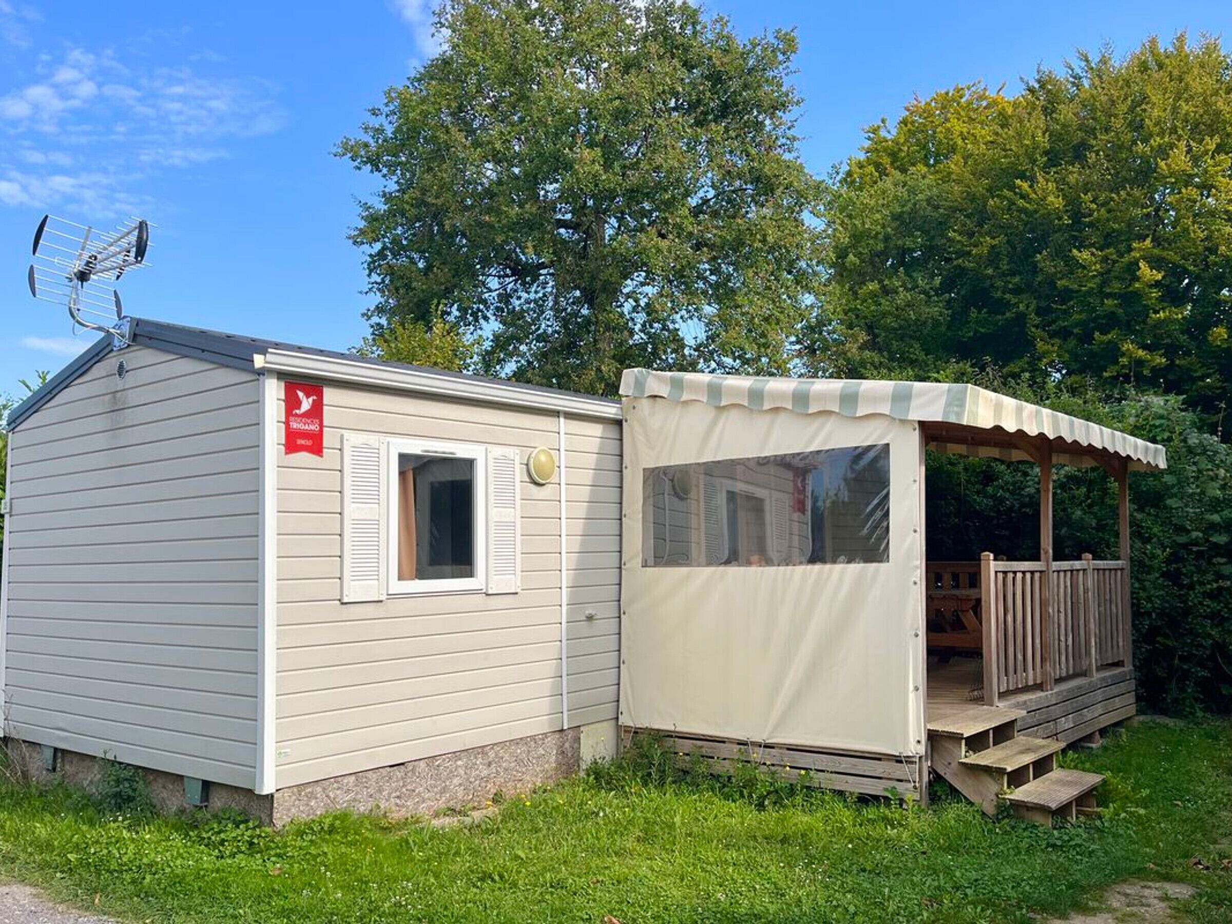 A small, single-story mobile home with a covered porch and a satellite dish.