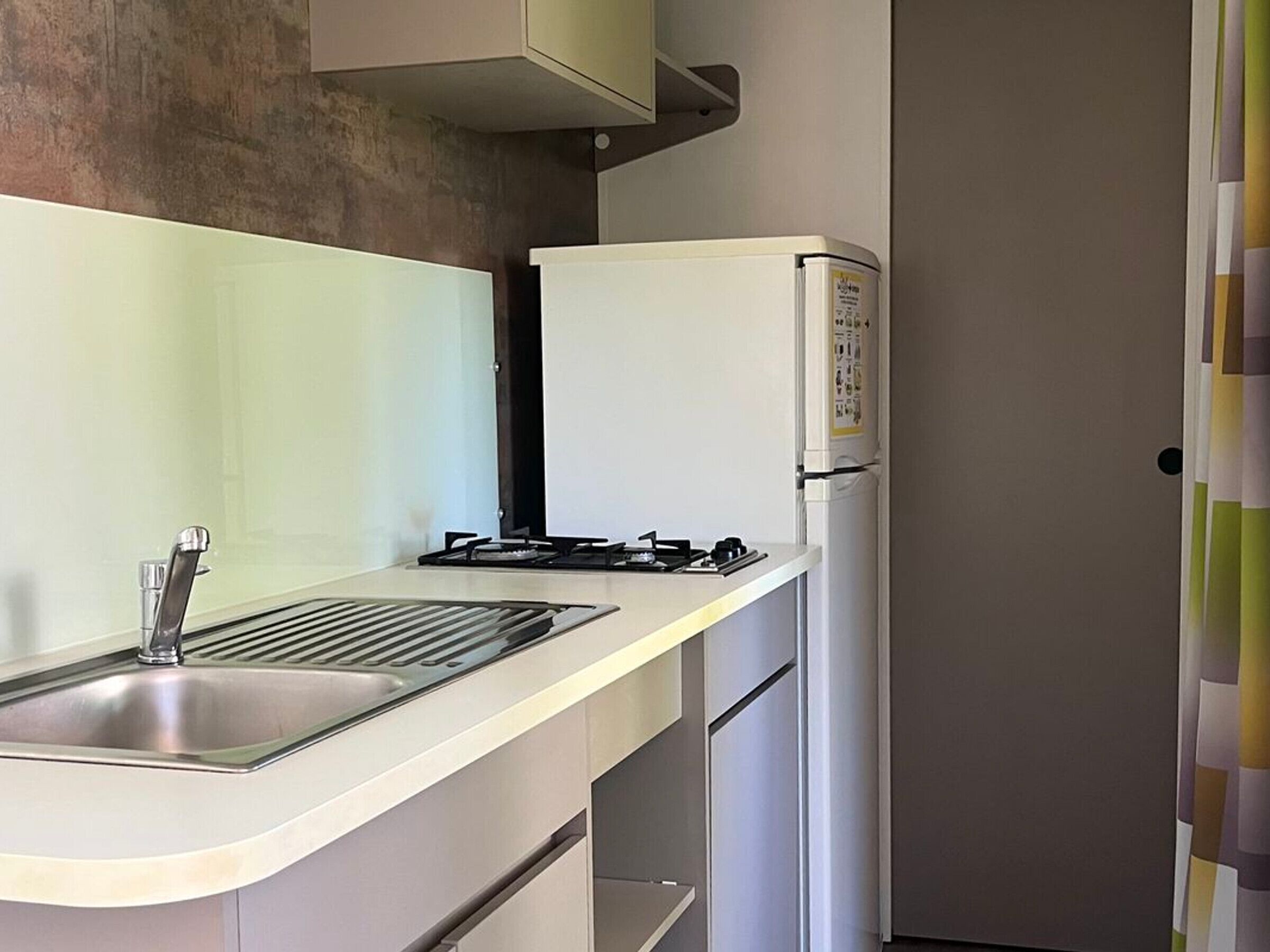 Una cocina compacta con un lavamanos de acero inoxidable, una estufa a gas y un refrigerador blanco.