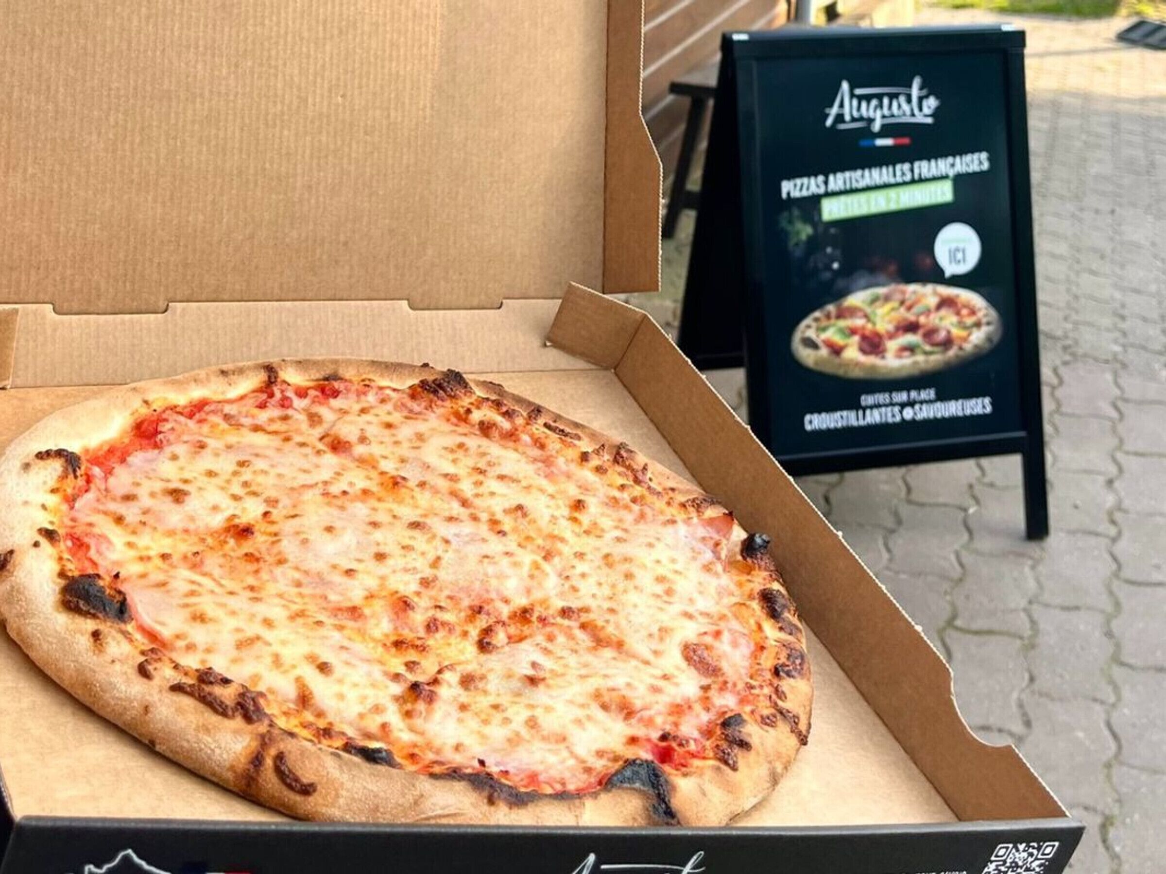 Une pizza dans une boîte en carton, avec un panneau de menu en arrière-plan.