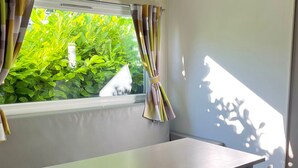 A room with a table and chairs, a window with curtains, and a view of greenery outside. - Mobile Home for 4 with Terrace (Angicourt)