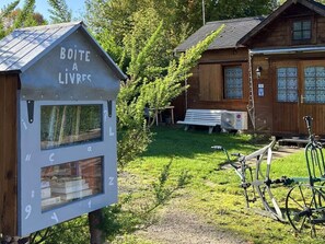 Una cabaña de madera con una pequeña biblioteca, señalizada como 'BOITE A LIVRES', y un aparcamiento para bicicletas.