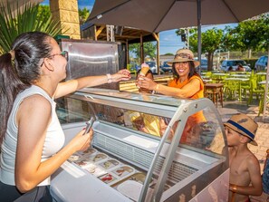 Un stand de vente de glaces en plein air, doté d’une structure en verre, où une personne sert des glaces et une autre personne tient un cornet.