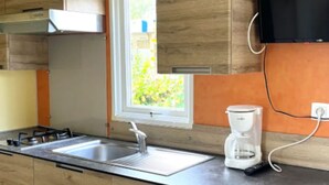 A modern kitchen with a stainless steel sink, a coffee maker, and wooden cabinets. - Family Mobile Home for 5 in Angicourt (Angicourt)