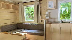 Une petite cuisine équipée, avec une cuisinière intégrée, un évier et une fenêtre avec des rideaux.